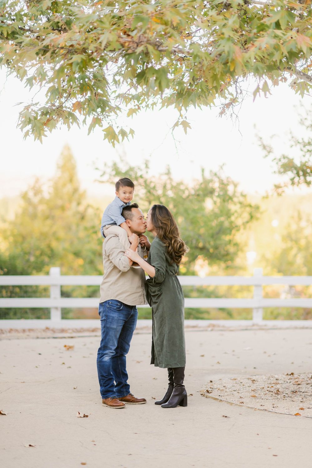 Young couple shares a tender moment on an autumn day under fall foliage near a white fence.