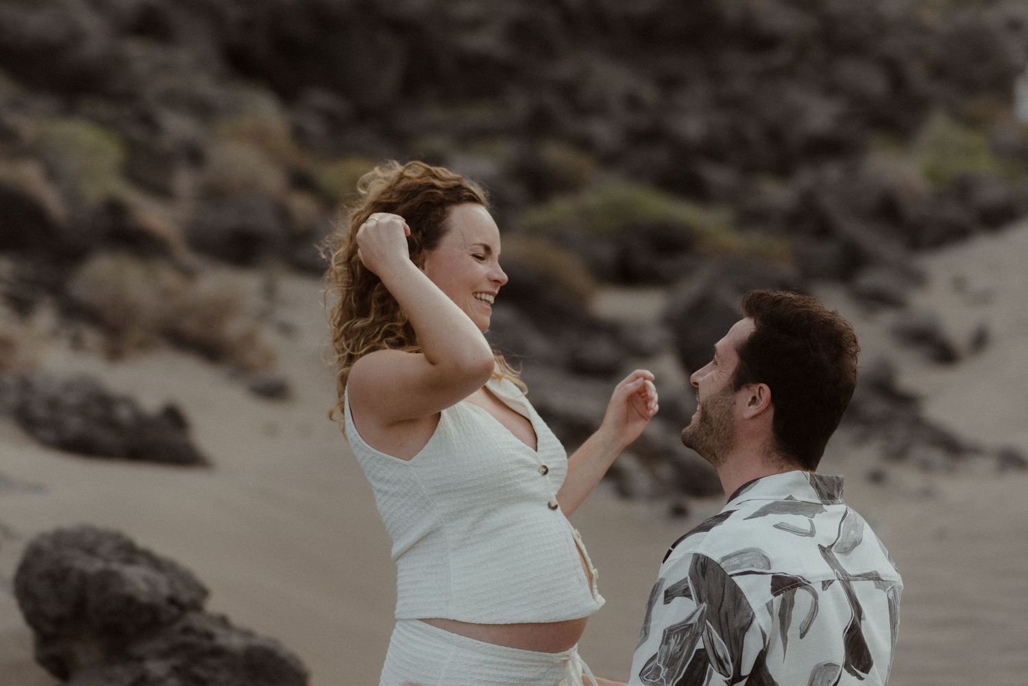 Happy couple shares a joyful moment together on a rocky beach during sunset.