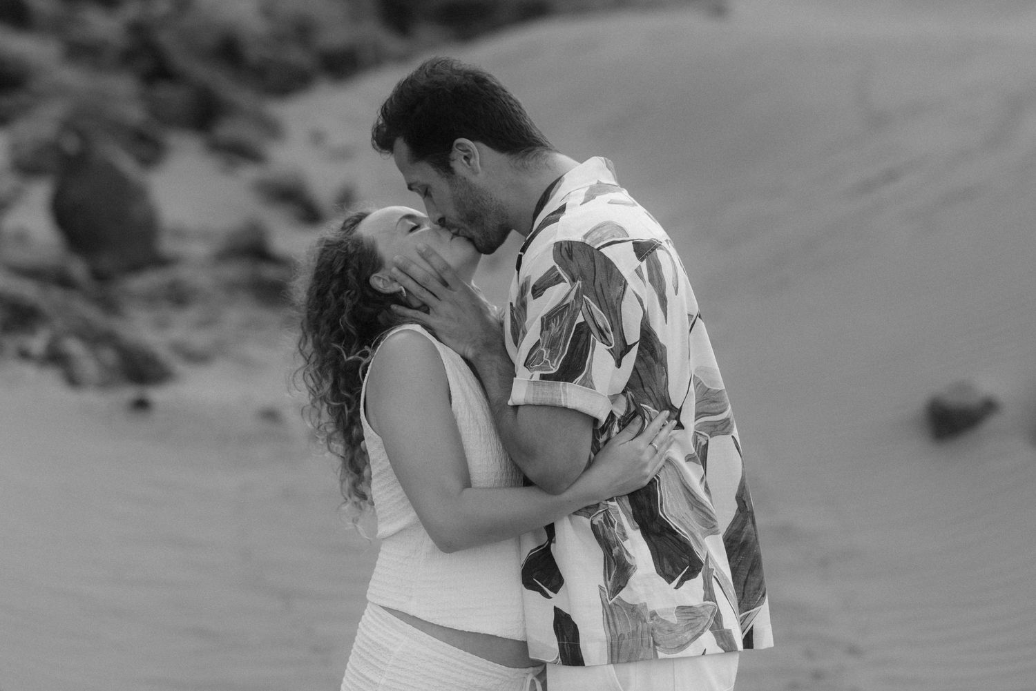 A romantic couple embraces on a sandy beach in black and white photography.