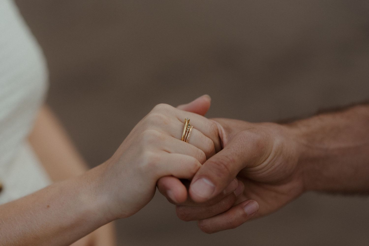 Two hands tenderly grasp each other with one person wearing a gold wedding band in a soft, intimate moment.