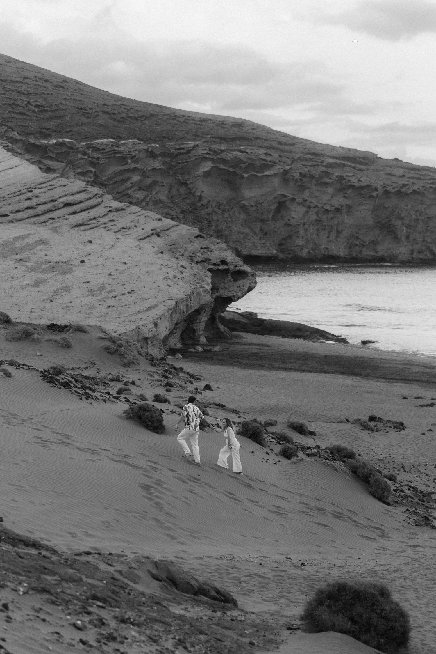 Black and white landscape photos show people walking on a rugged volcanic beach coastline with steep cliffs and crashing waves.
