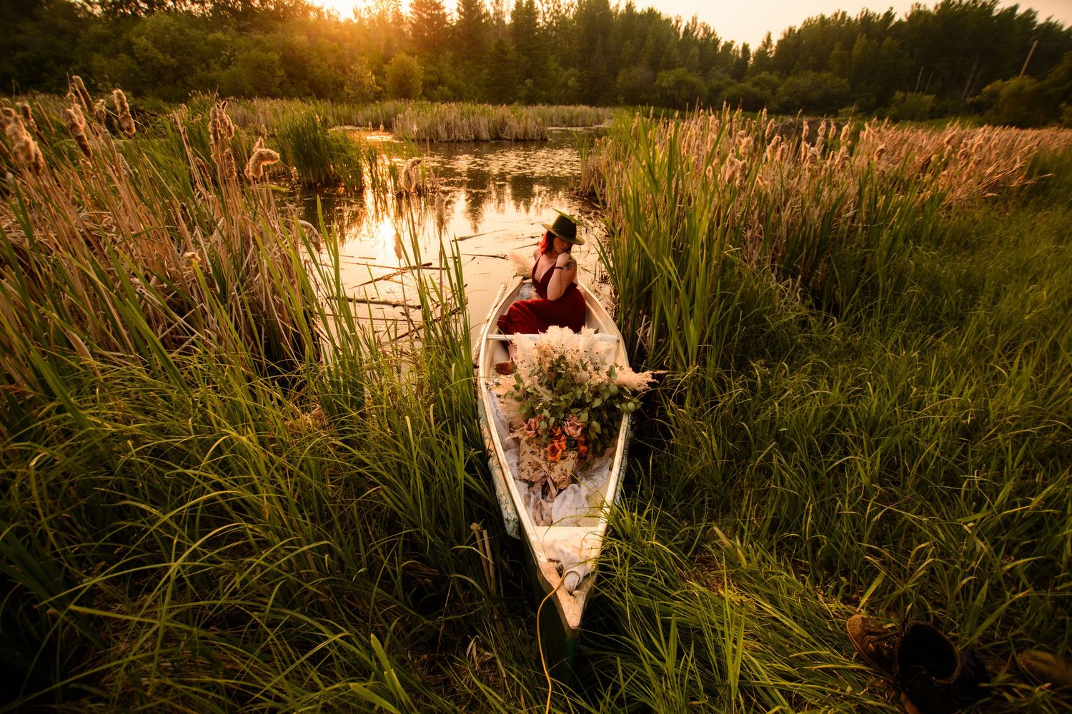 A person walks through a tranquil marsh landscape during a golden sunset with tall reeds and water reflections.