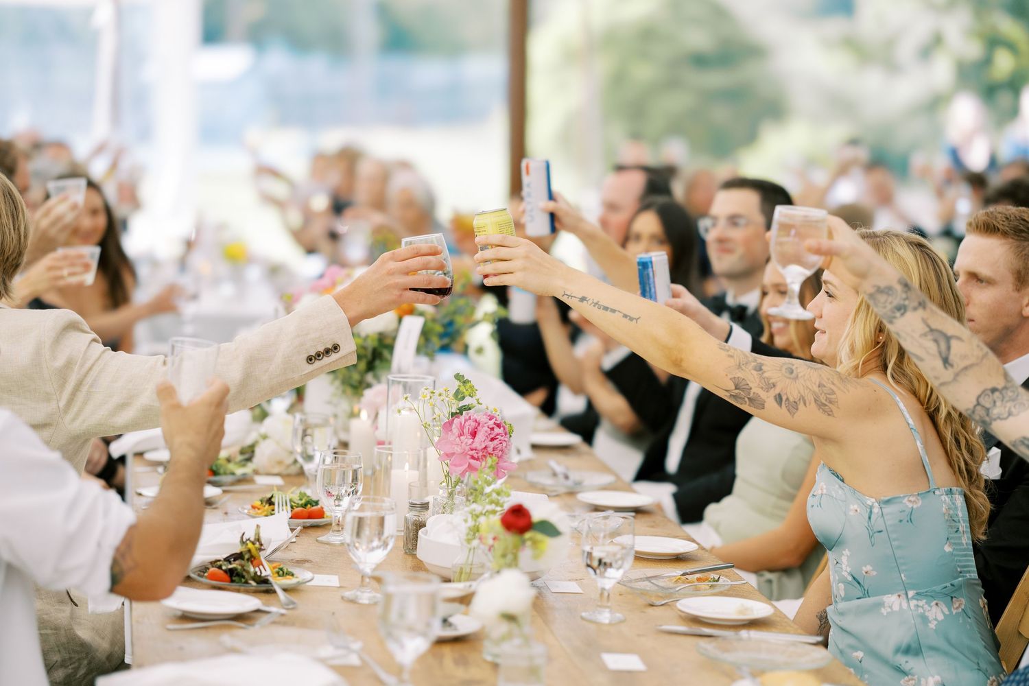 Wedding guests in formal attire raise their glasses for a celebratory toast at an elegant reception table decorated with pink flowers.