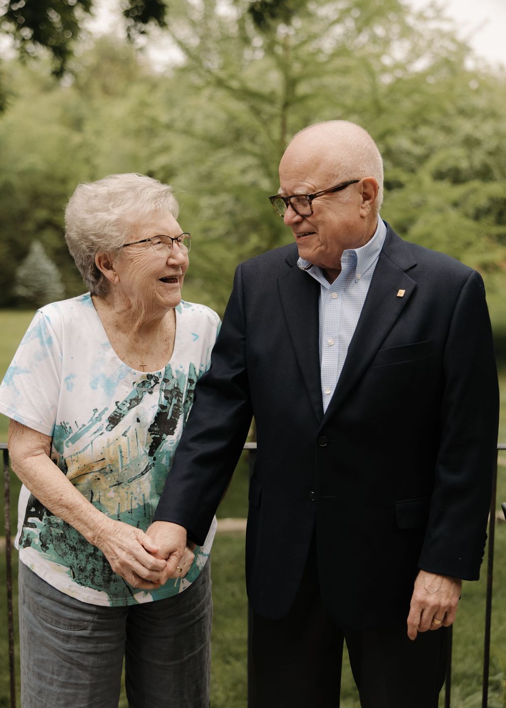 Elderly couple sharing a joyful laugh together outdoors while dressed in casual and formal attire.