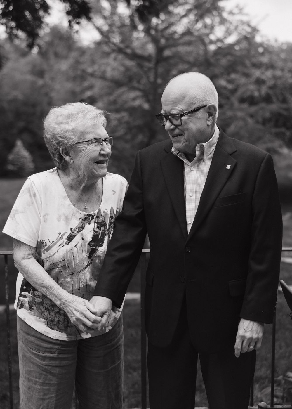 Black and white photo of elderly couple sharing a joyful candid moment as they smile and laugh together outdoors.