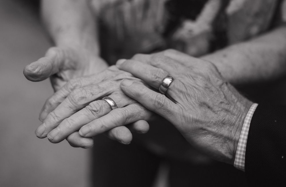 A black and white image showing elderly wrinkled hands clasping together in a tender pose.