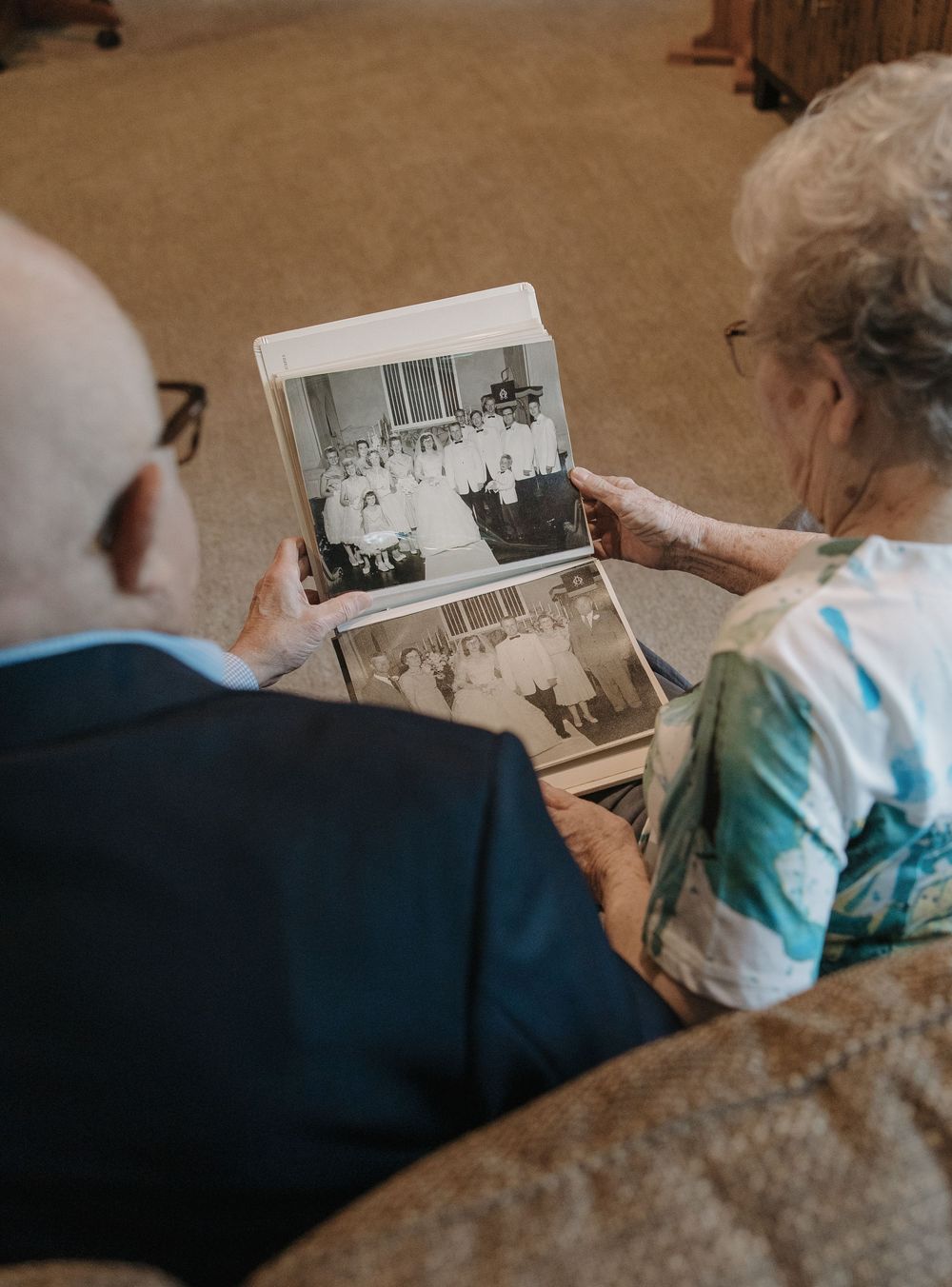 An elderly couple looks through vintage black and white photographs together while sitting on a couch.
