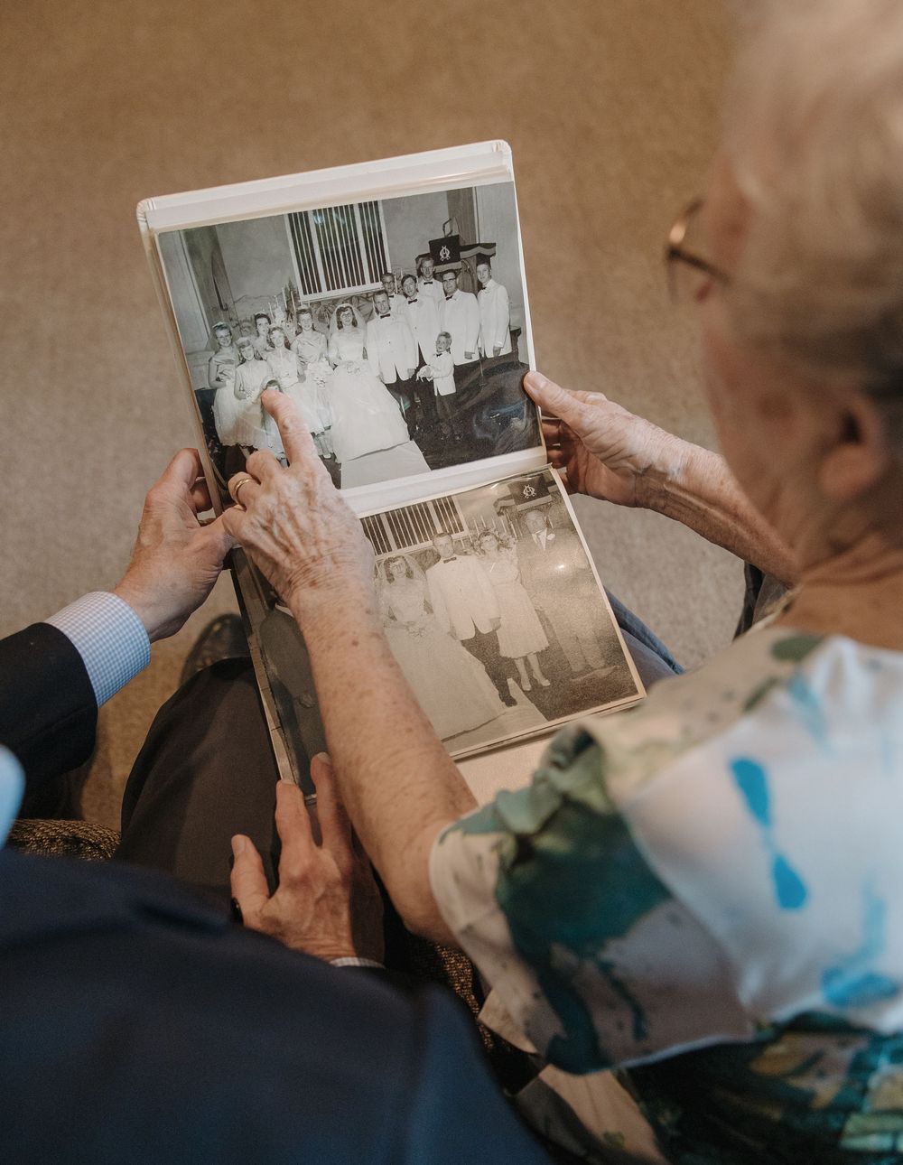 Elderly hands holding an old photo album while looking at black and white photographs from the past.