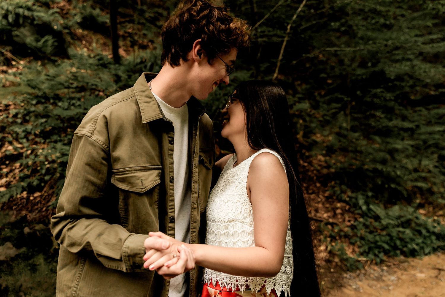 Romantic outdoor photo of a couple sharing an intimate moment in nature wearing casual clothing against a forest background.