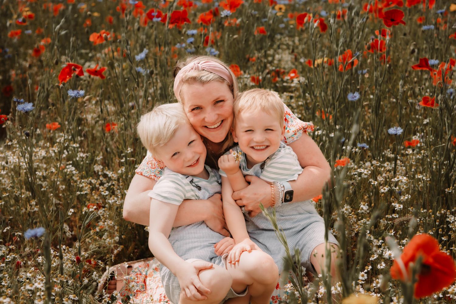 Three people sharing a joyful moment together in a vibrant field of red poppies and white wildflowers.