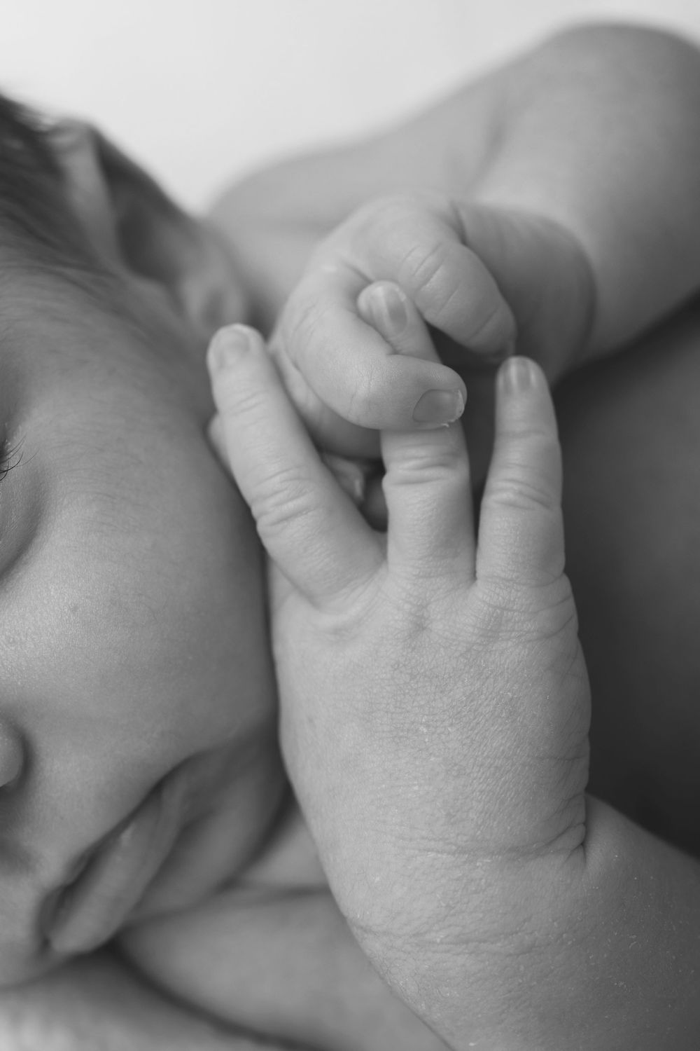A close-up black and white photo of a baby's tiny hand gently grasping an adult finger.