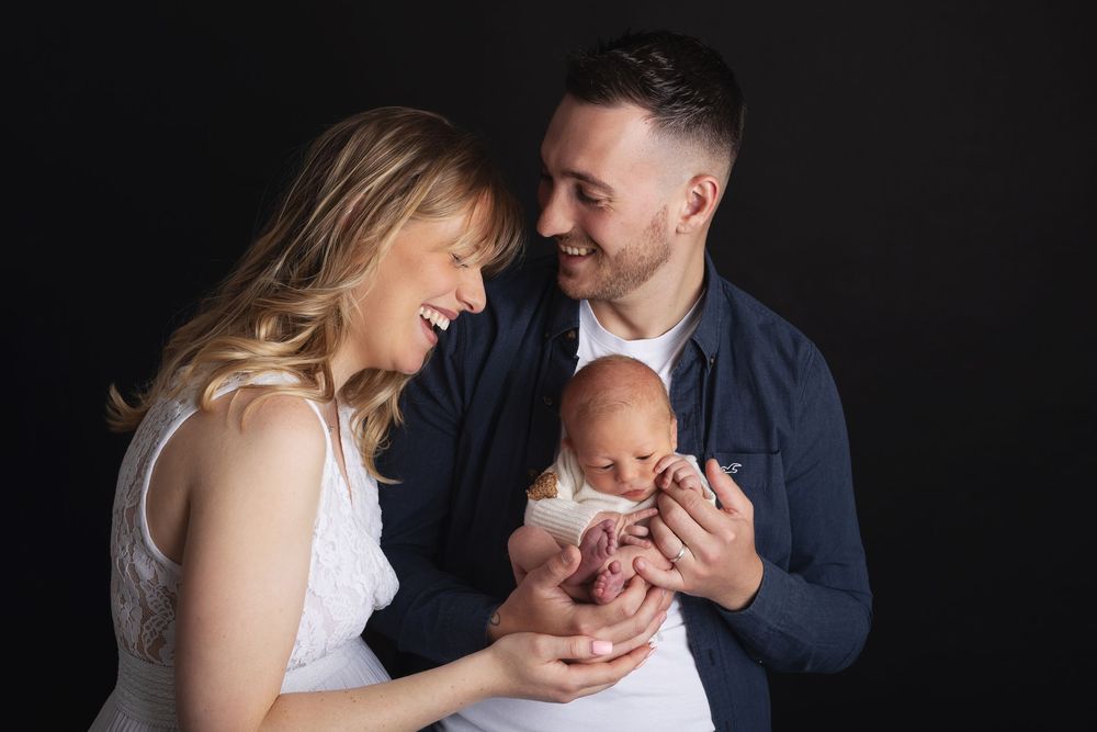 A couple shares a joyful moment with their newborn baby against a dark background.