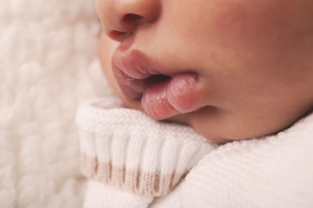 Close-up macro shot of baby's lips and nose against soft white knitted fabric in natural lighting.