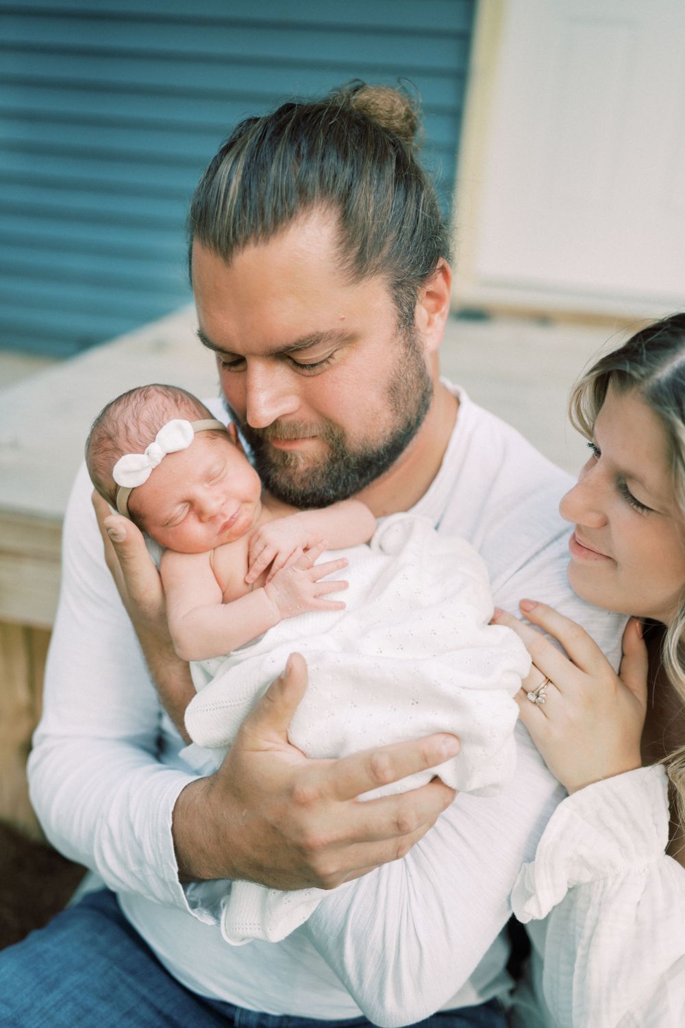 Peaceful family moment with sleeping newborn baby in white outfit outdoors.