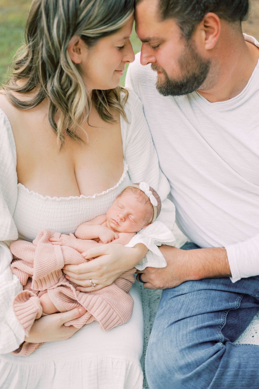 A tender moment between parents as they cradle their newborn baby in a soft pink blanket outdoors.