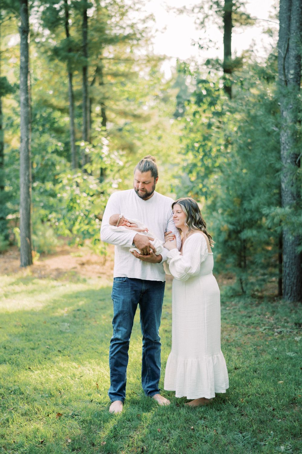 Parents standing in sunlit forest clearing while holding their newborn baby.