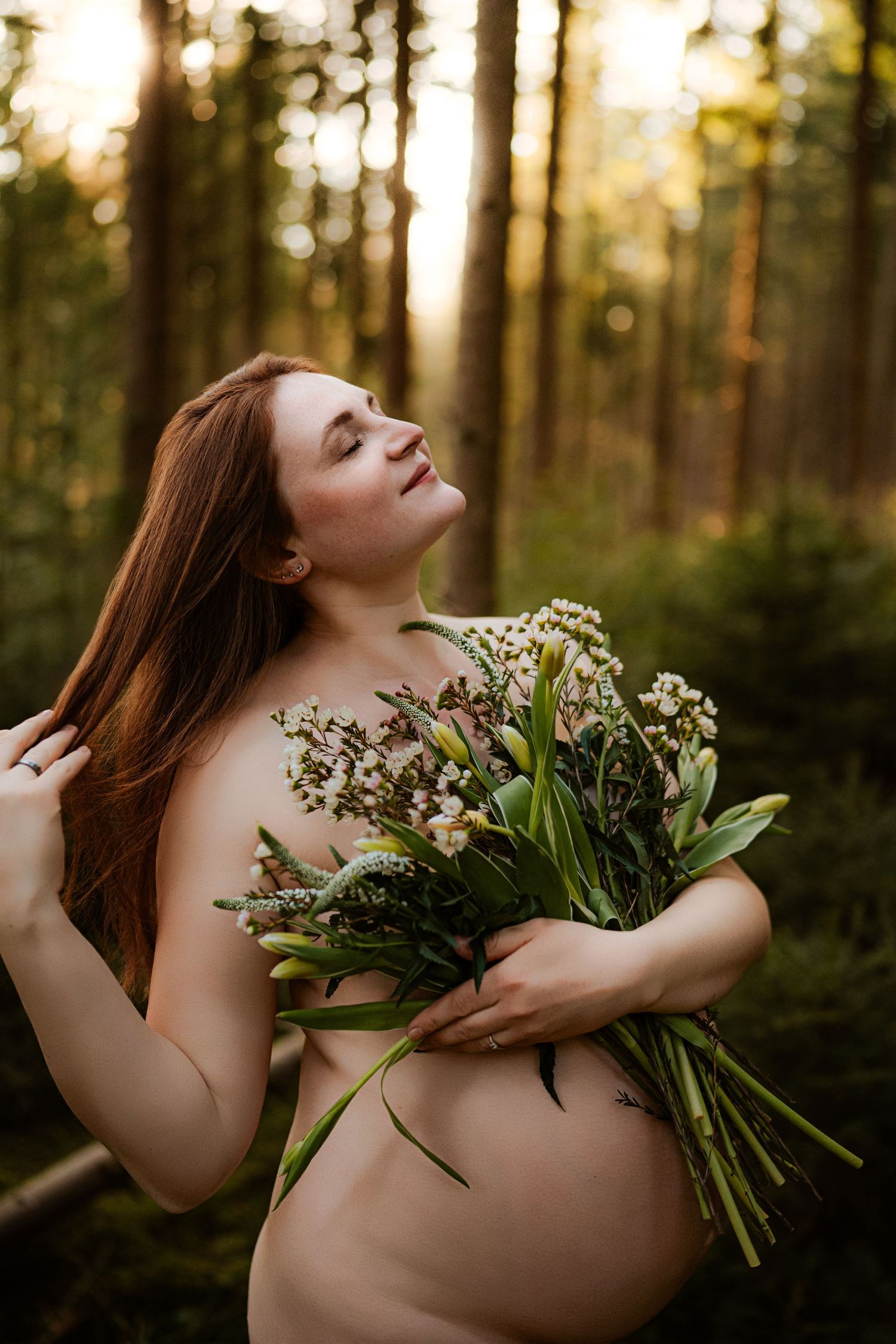 A figure poses gracefully with a bouquet of white lilies and greenery in a sunlit forest during golden hour.