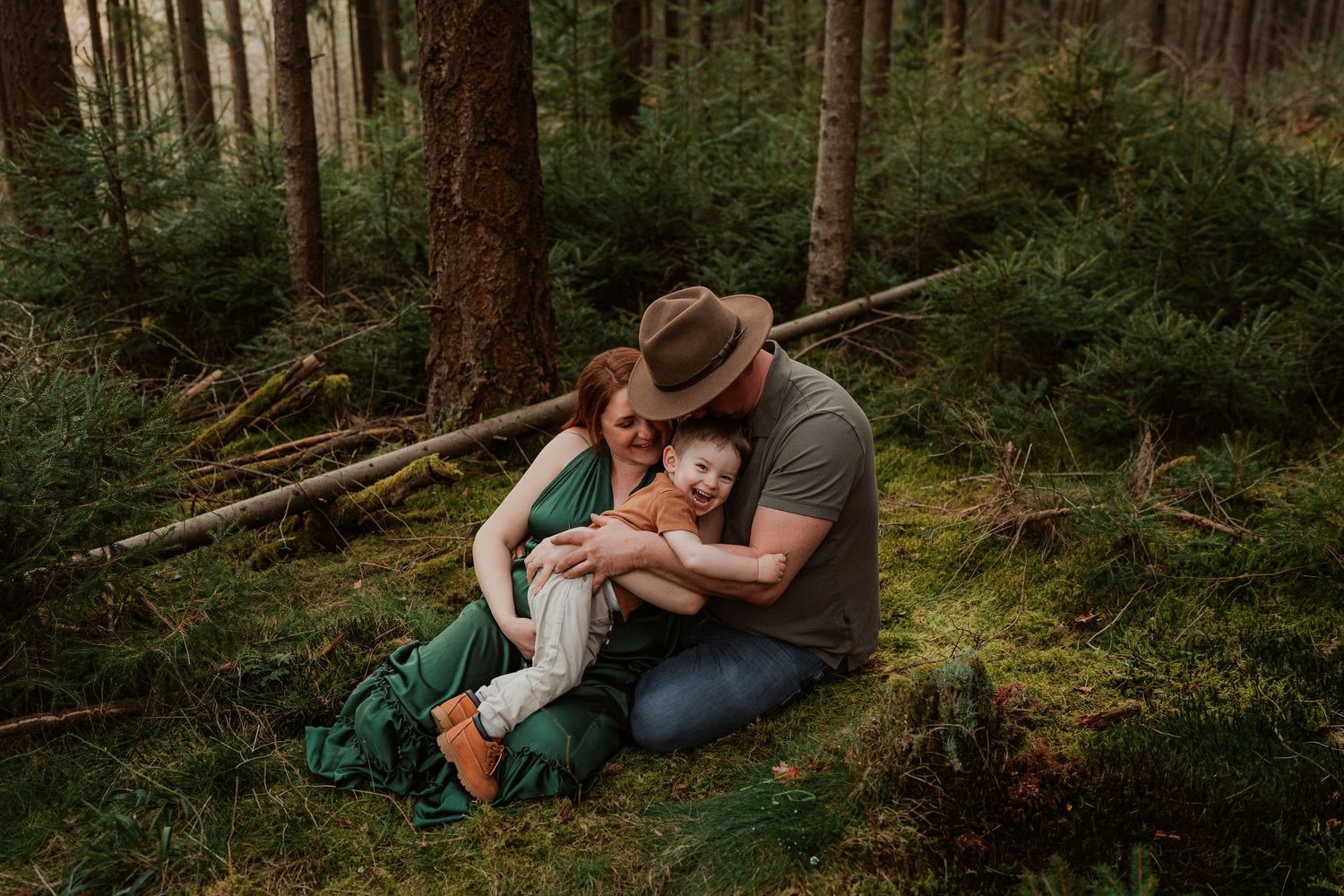 Intimate outdoor scene of couple embracing on forest floor surrounded by evergreen trees and moss.