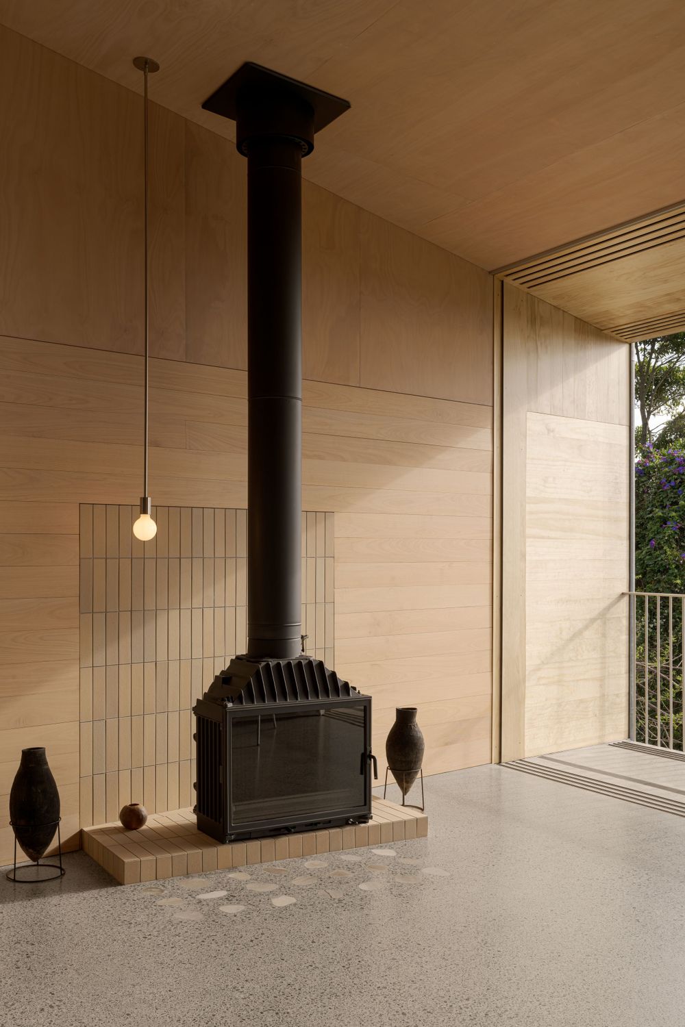 Black wood-burning fireplace with pendant light in modern room with beige walls and glass panels.