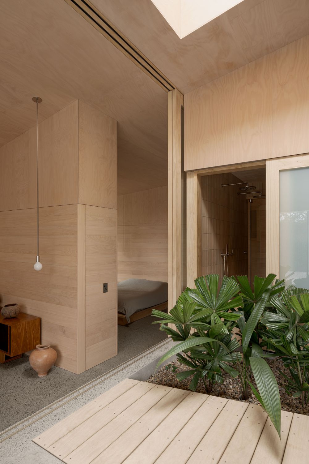 Minimalist indoor-outdoor space with beige tiles and lush green plants in a built-in garden bed.