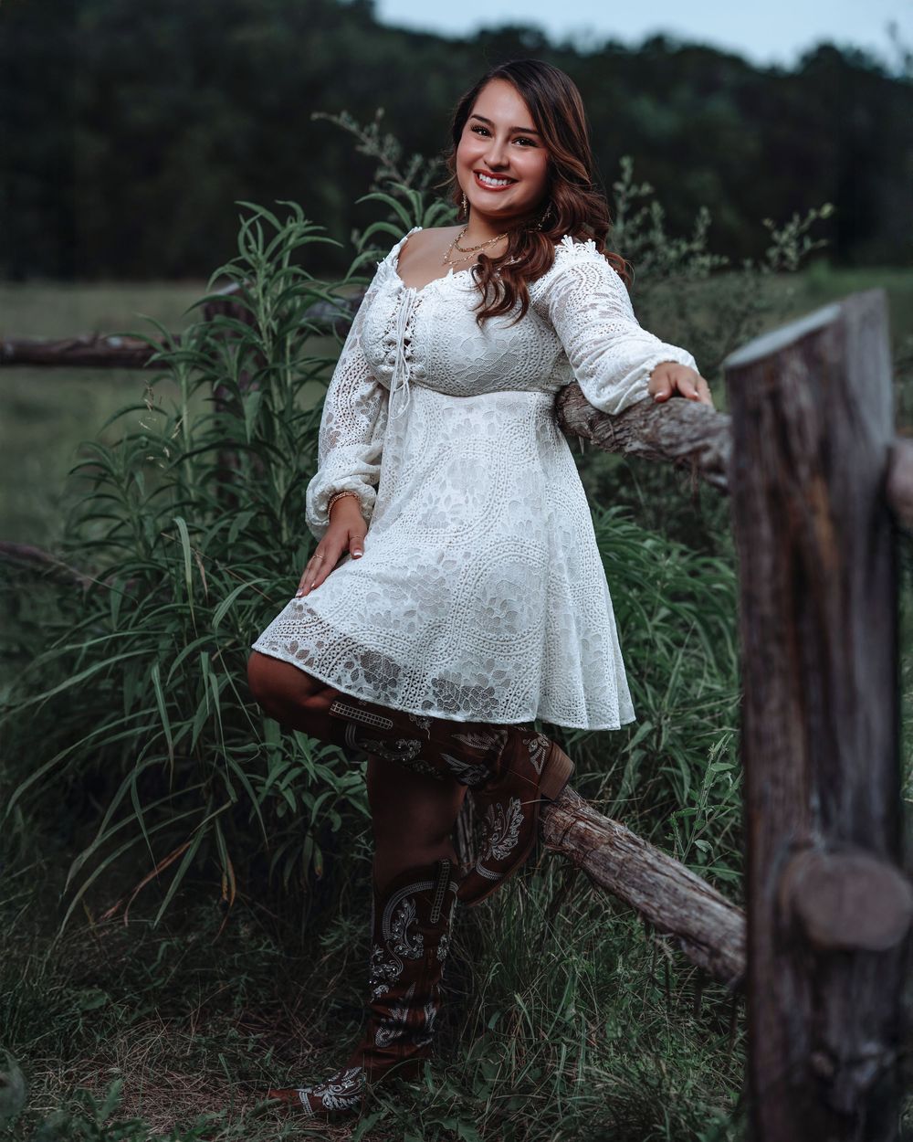 White lace dress and brown cowboy boots create a country chic style against a rustic fence and natural backdrop.