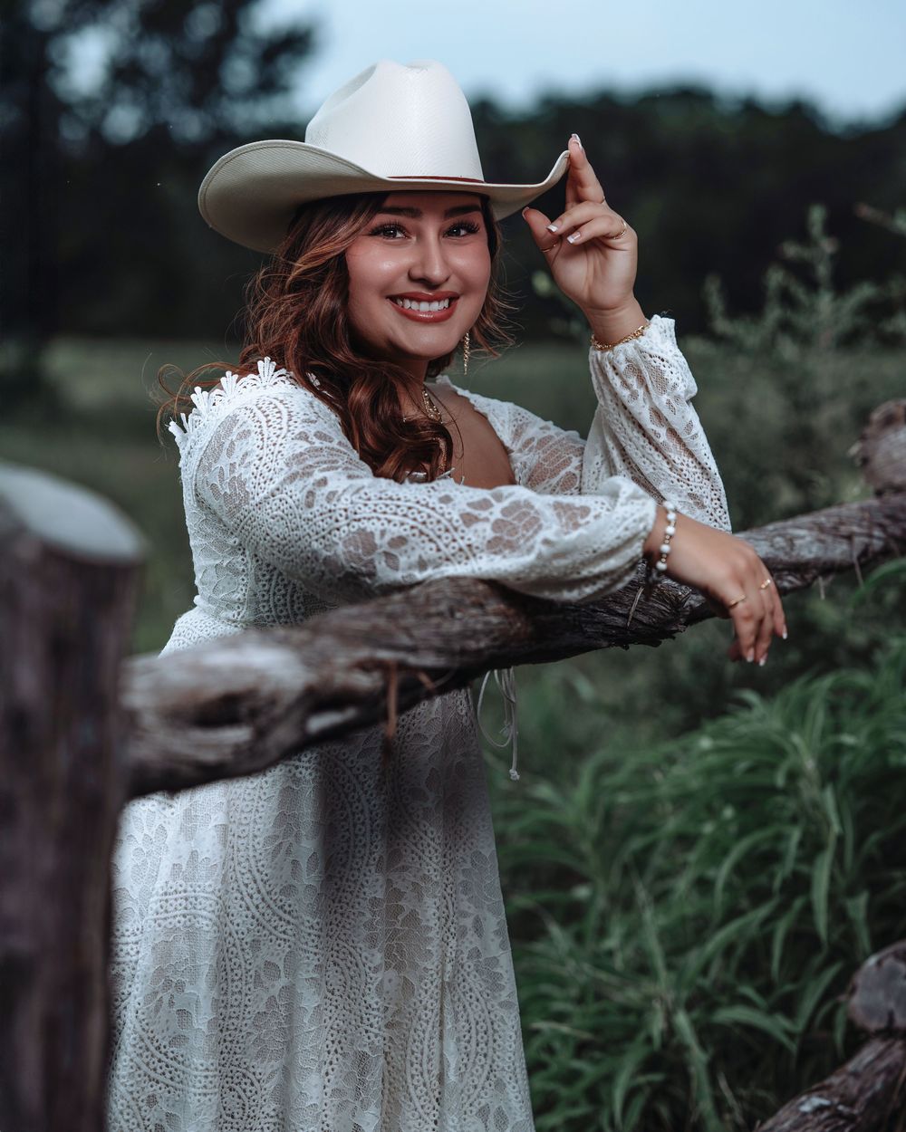 A dreamy portrait session in nature featuring a white lace dress and cowboy hat against a rustic outdoor backdrop.