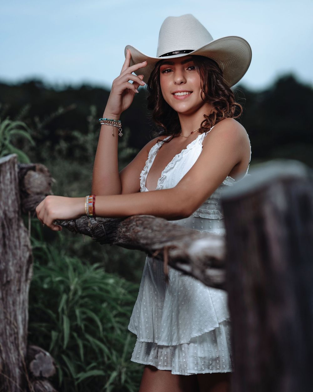 Outdoor fashion photography with a western theme showing a flowy white dress and cowboy hat at golden hour.