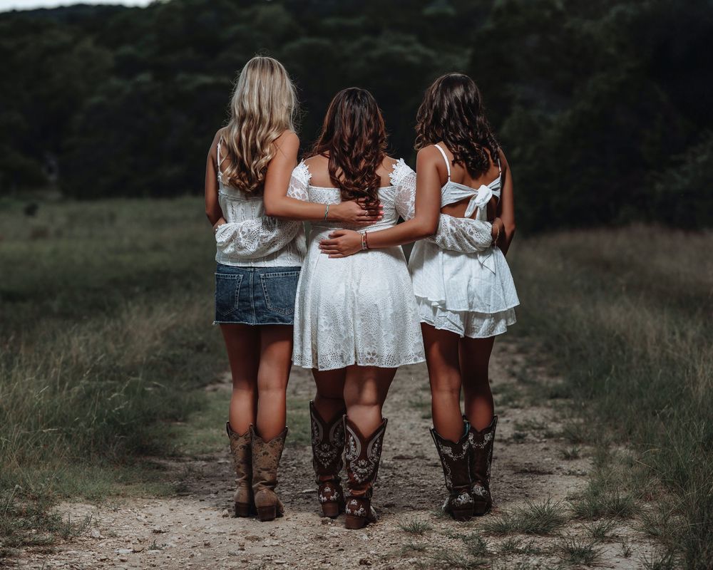 Three people in matching white dresses and brown boots walking together on a dirt path.