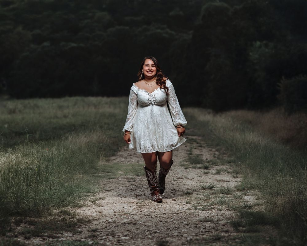 A stylish white dress and brown boots complement a rustic country path at dusk.