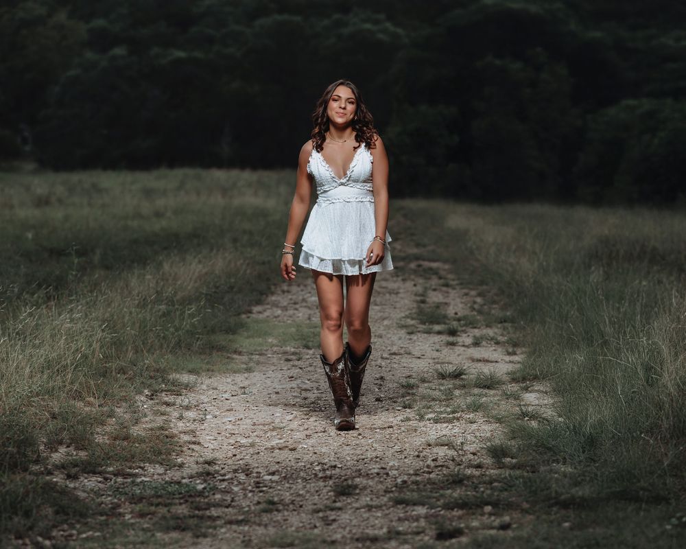 A white summer dress paired with cowboy boots creates a country chic look on a dirt path.