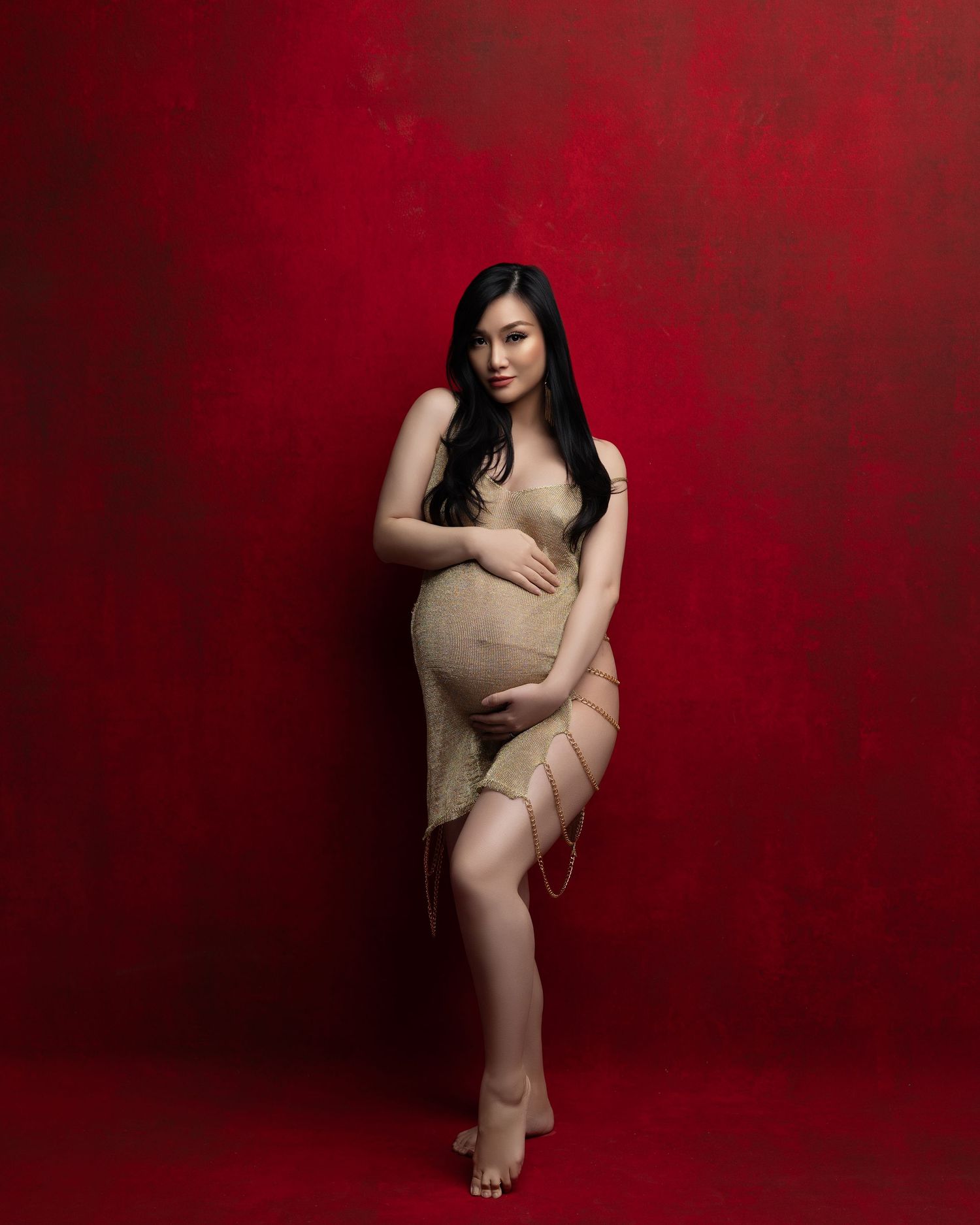 Artistic maternity portrait against a deep red background featuring elegant draping fabric and dramatic lighting.