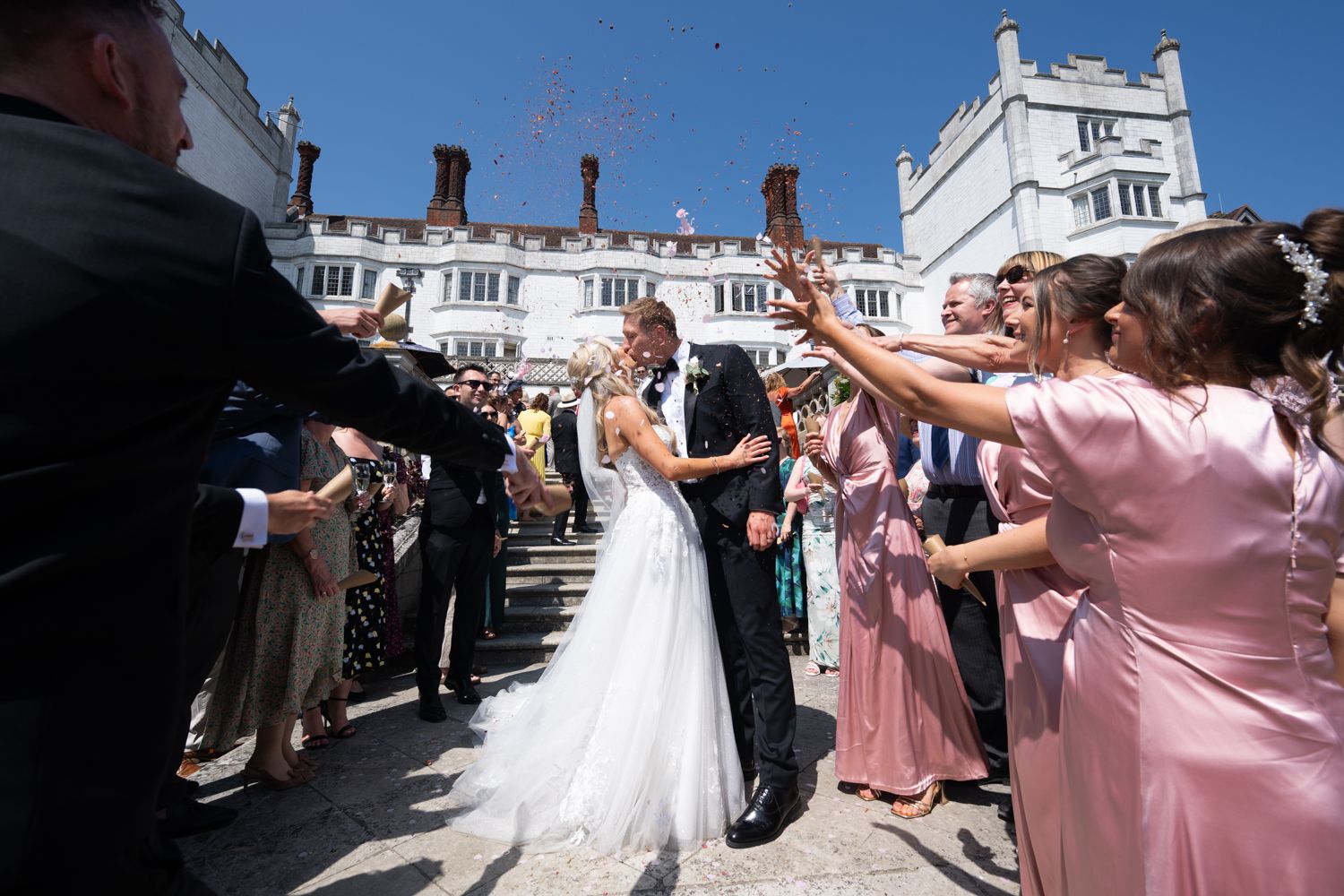 Wedding celebration at a stately white building as guests toss confetti over the couple.