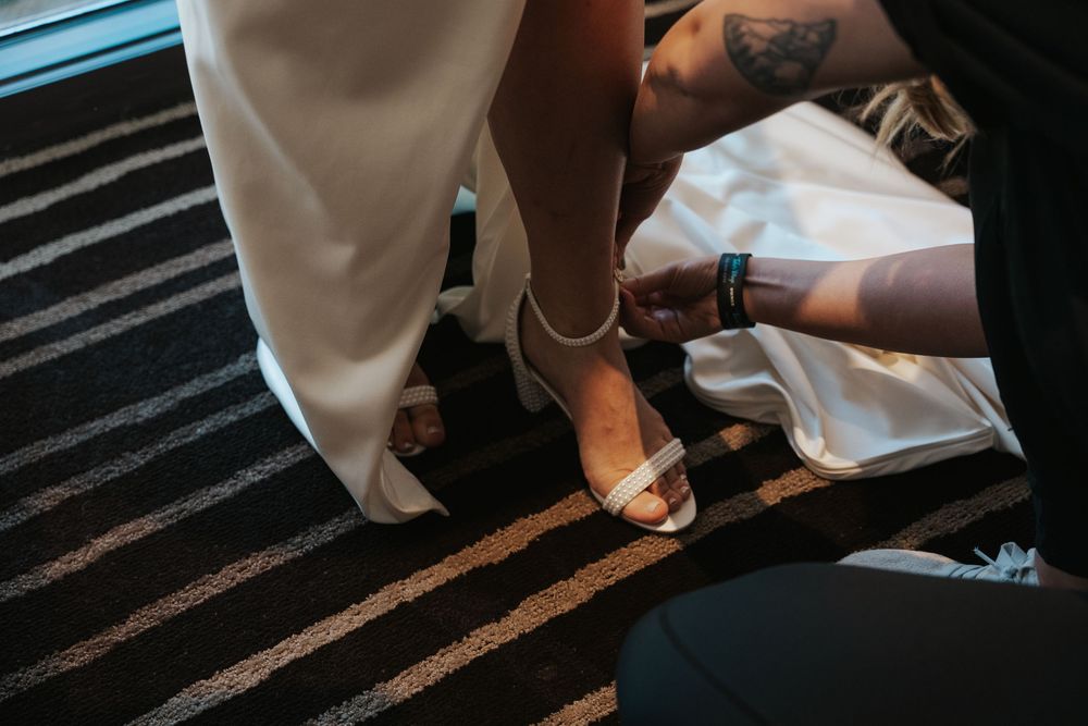 A person wearing white lace sandals steps across a dark striped surface at a wedding ceremony.