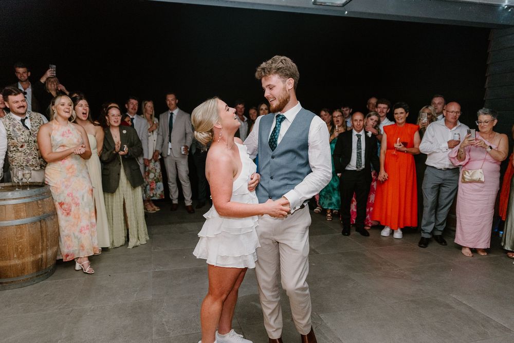 Couple shares their first dance surrounded by guests at a rustic winery reception venue.