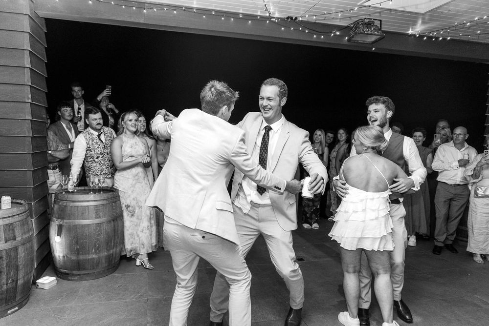 Black and white photo of people dancing at a casual party with wooden barrels visible in the background.