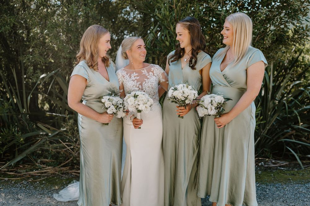 Wedding party wearing sage green bridesmaid dresses pose with bouquets in an outdoor garden setting.