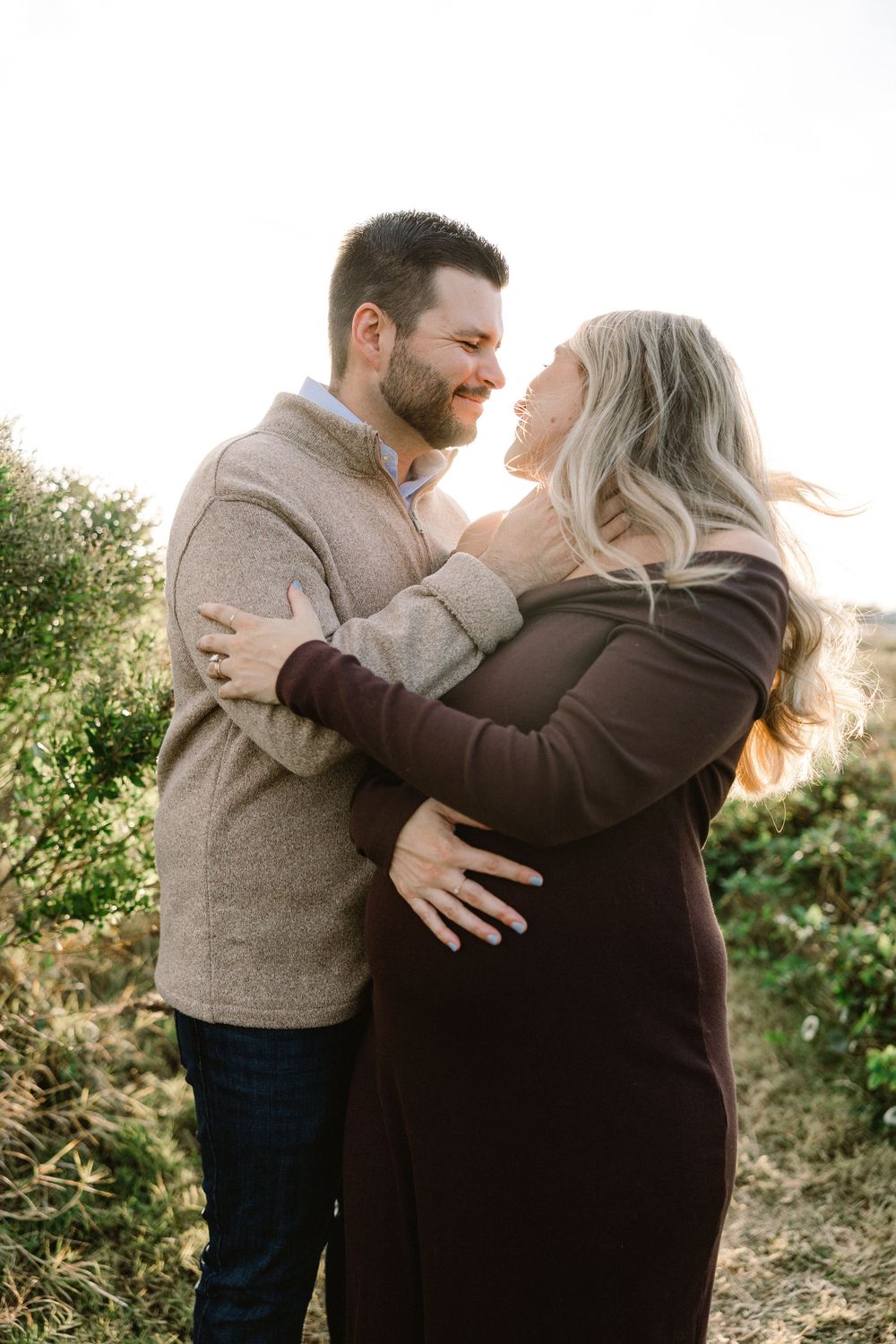 Candid maternity photo of expecting couple embracing outdoors at sunset.