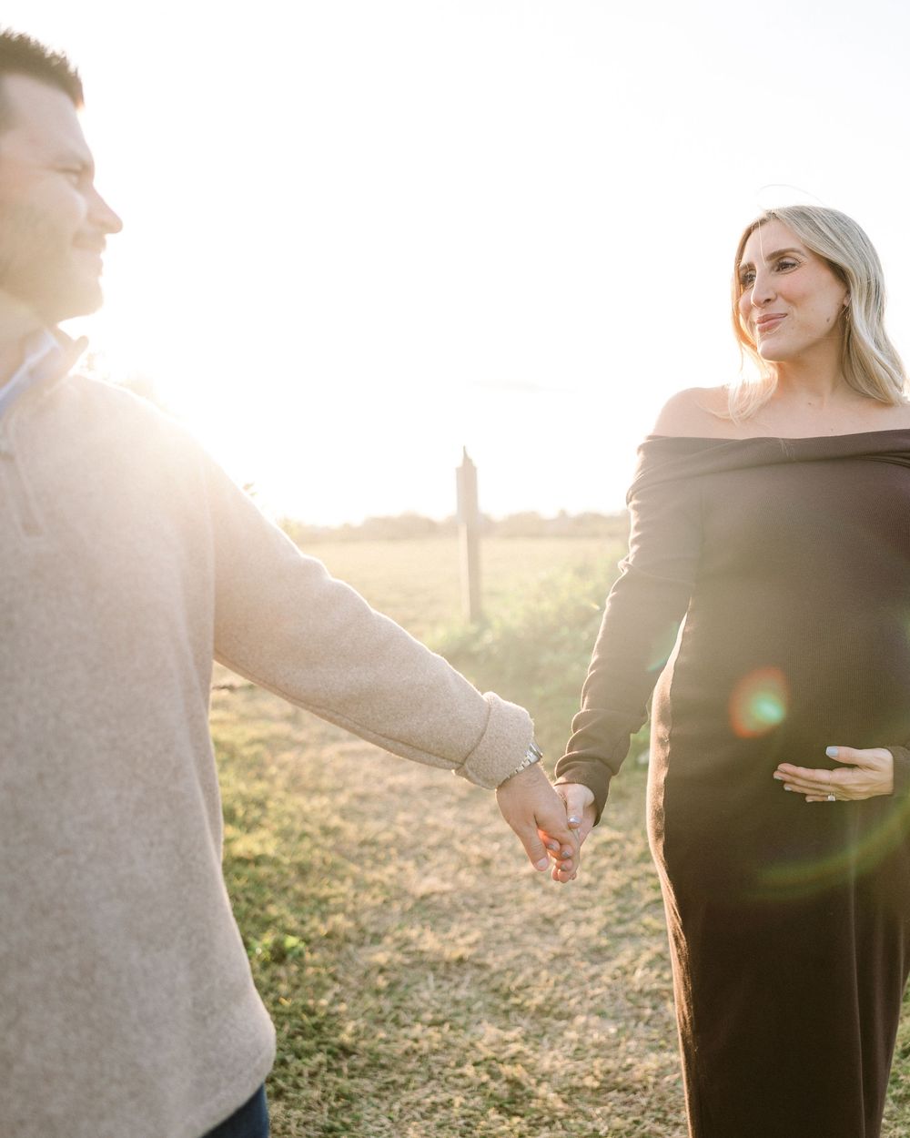 Expecting couple holding hands in golden sunlight with lens flare.