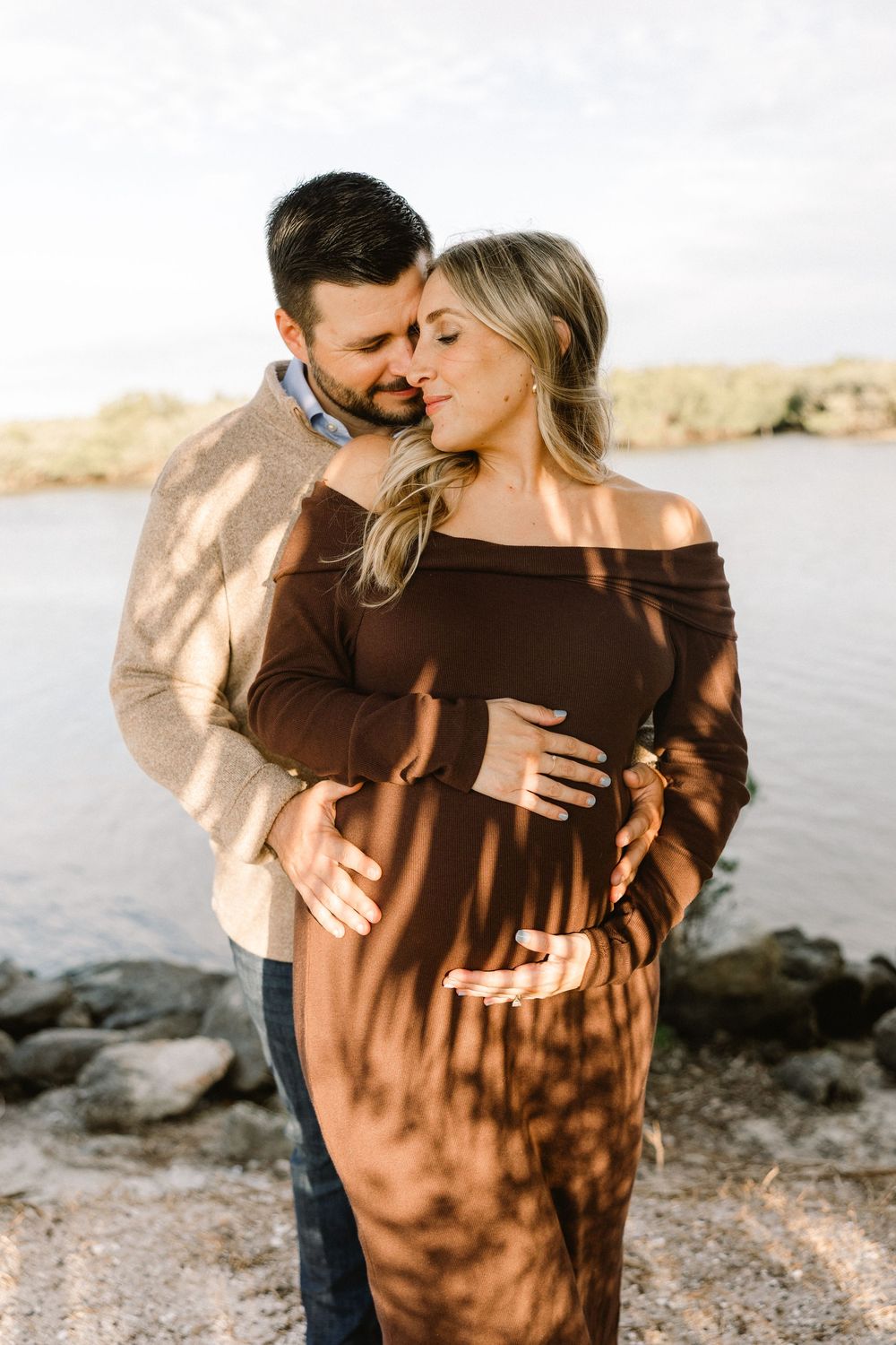 Romantic maternity portrait by water with dappled sunlight.