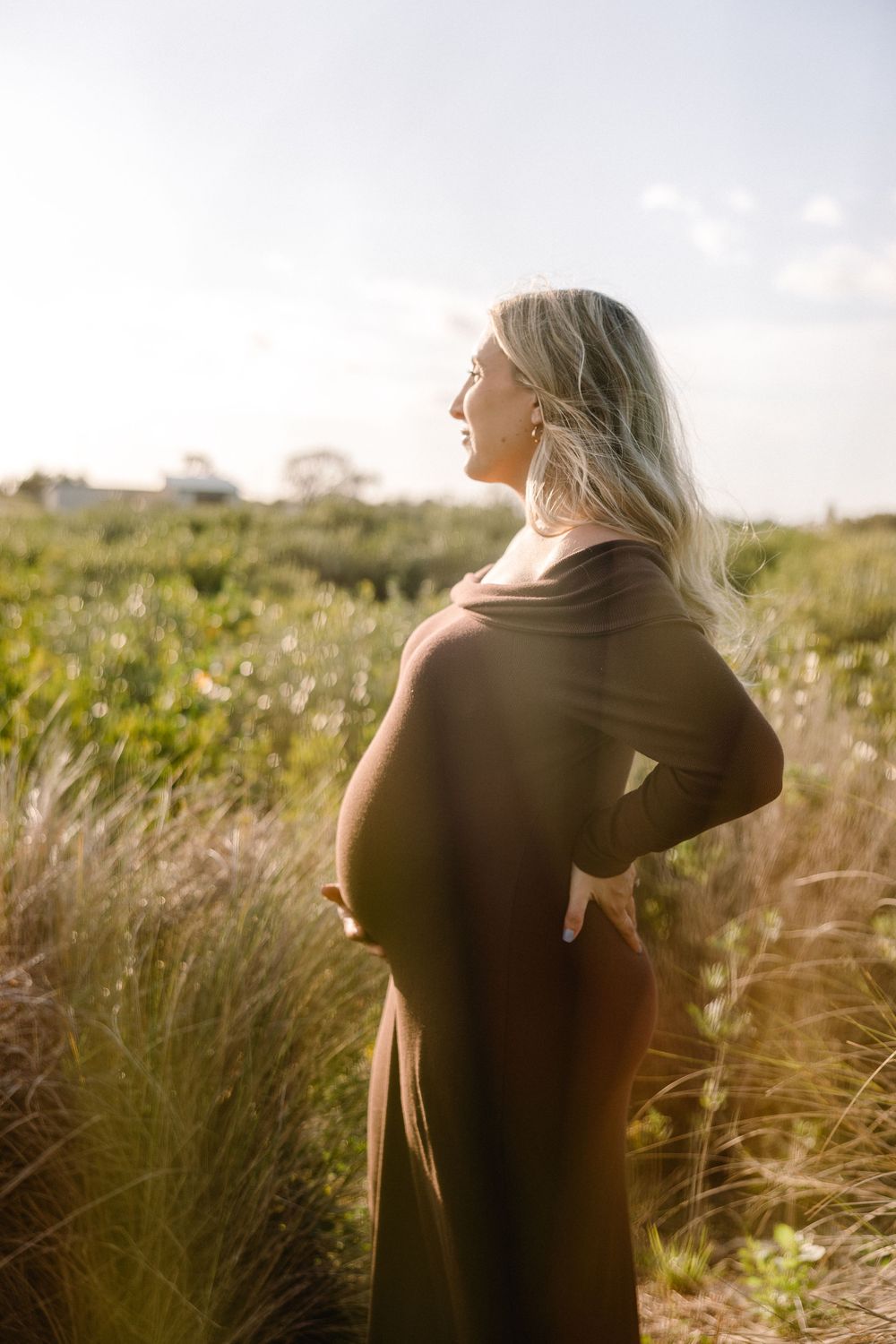 Side profile maternity silhouette in natural field setting at sunset.