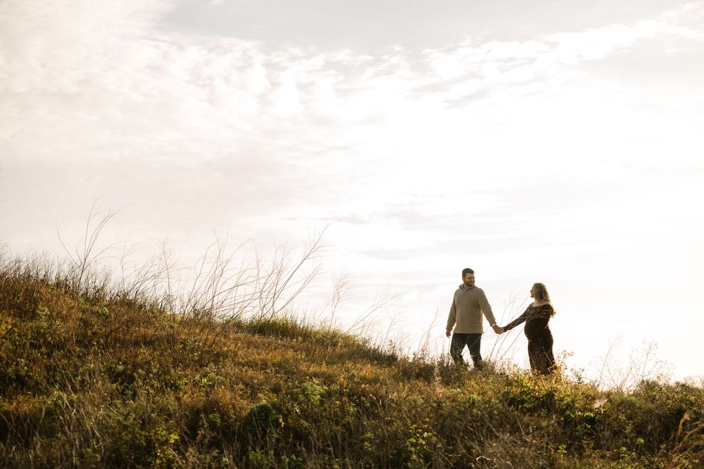 Silhouette of couple walking hand in hand on hilltop at sunset.