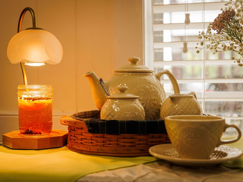 A cozy tea setting with a vintage teapot, cup, and warm glowing lamp illuminating a jar on a wooden tray.