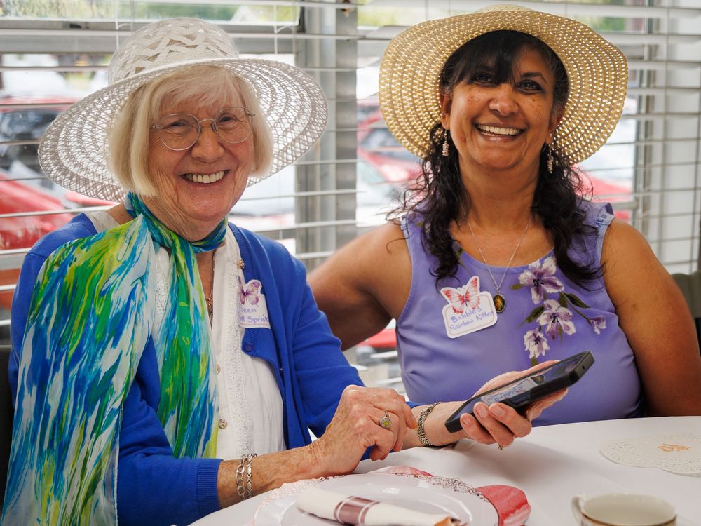 Two friends wearing sun hats share a joyful moment while dining together at an outdoor table.