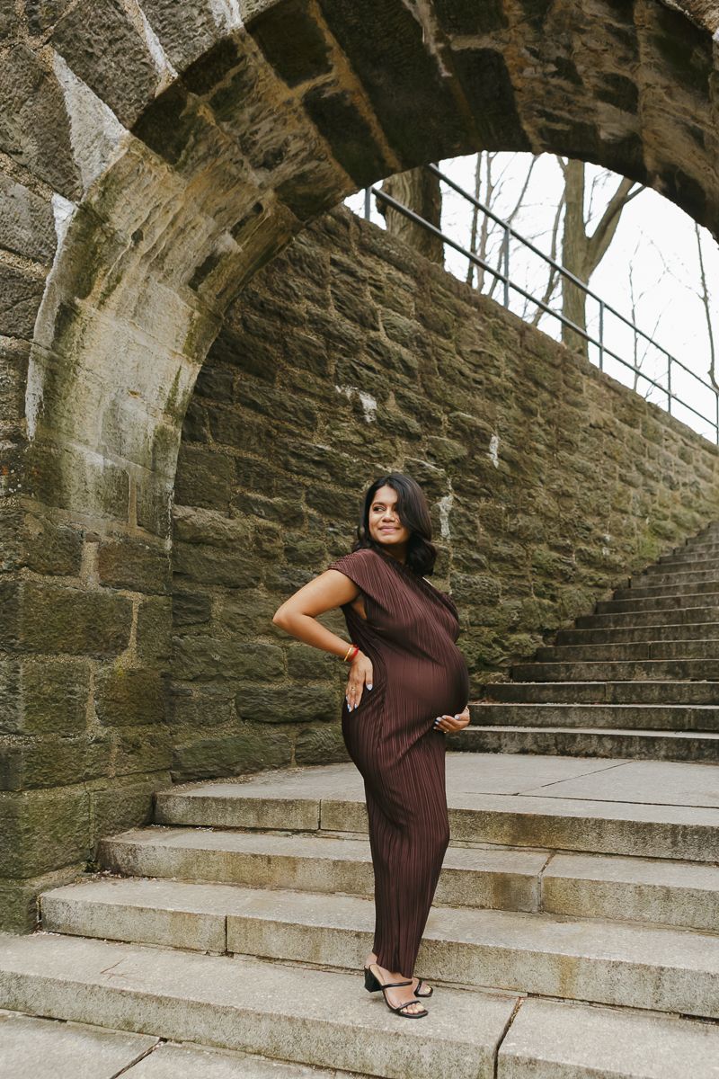 Serene profile of expecting mother under the grand arch at Fort Tryon Park, capturing timeless elegance by Paula Brearley NYC Maternity