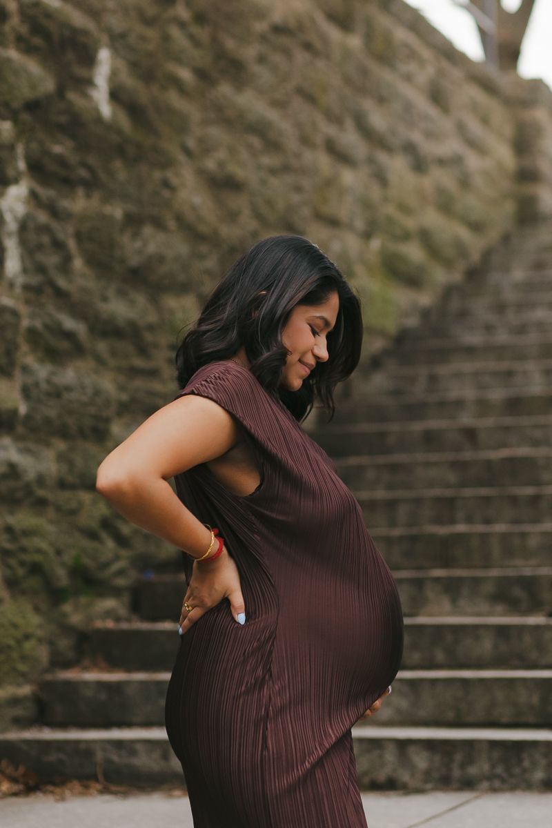 Soft close-up of mom-to-be’s profile, tenderly holding her baby bump, surrounded by Fort Tryon Park’s spring beauty by Paula Brearley