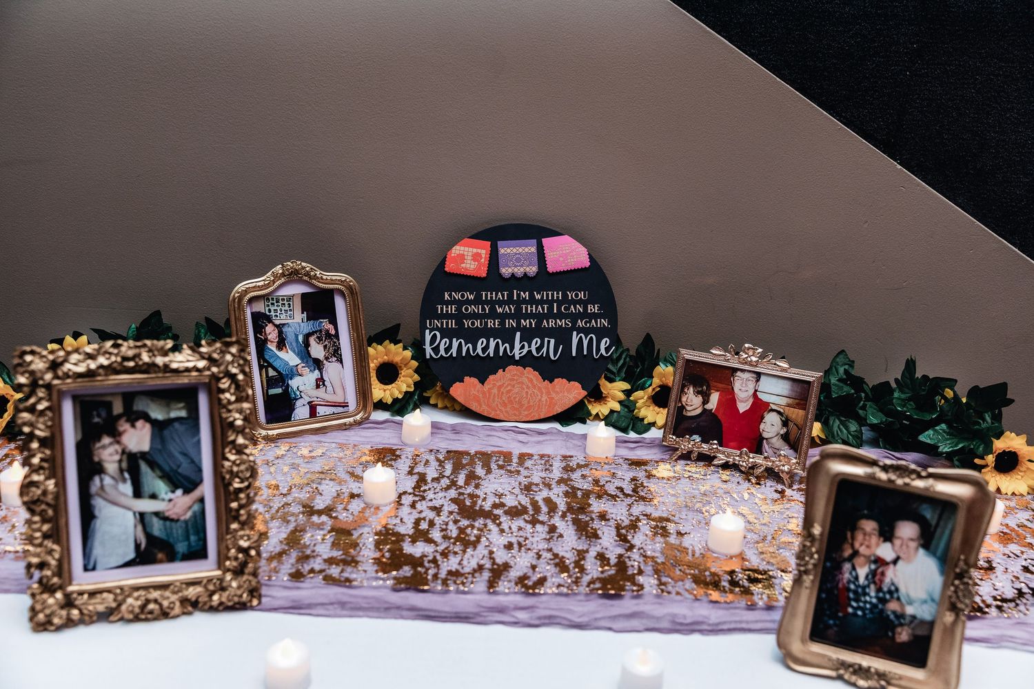 Wedding memorial display with framed photographs and decorative elements on white table with backlit lighting.