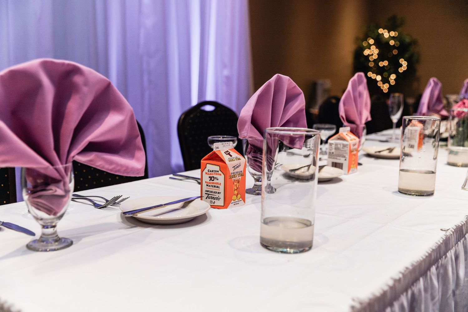 Elegant table setting with mauve napkins folded into fans, wine glasses, and white linens at a formal event.
