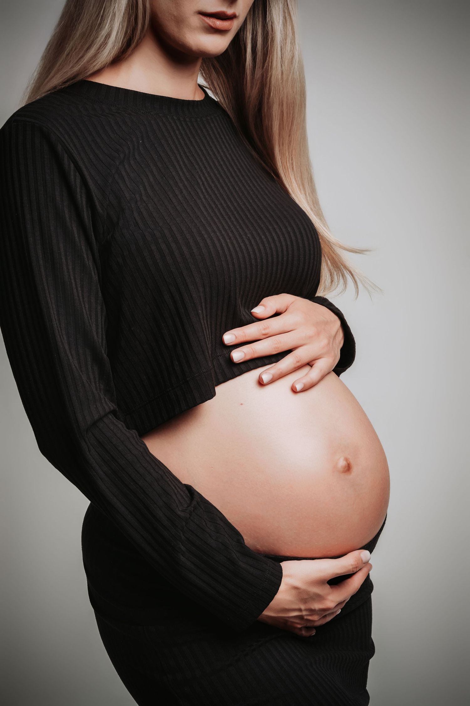 Maternity photo showing pregnant belly in black ribbed sweater against grey background.