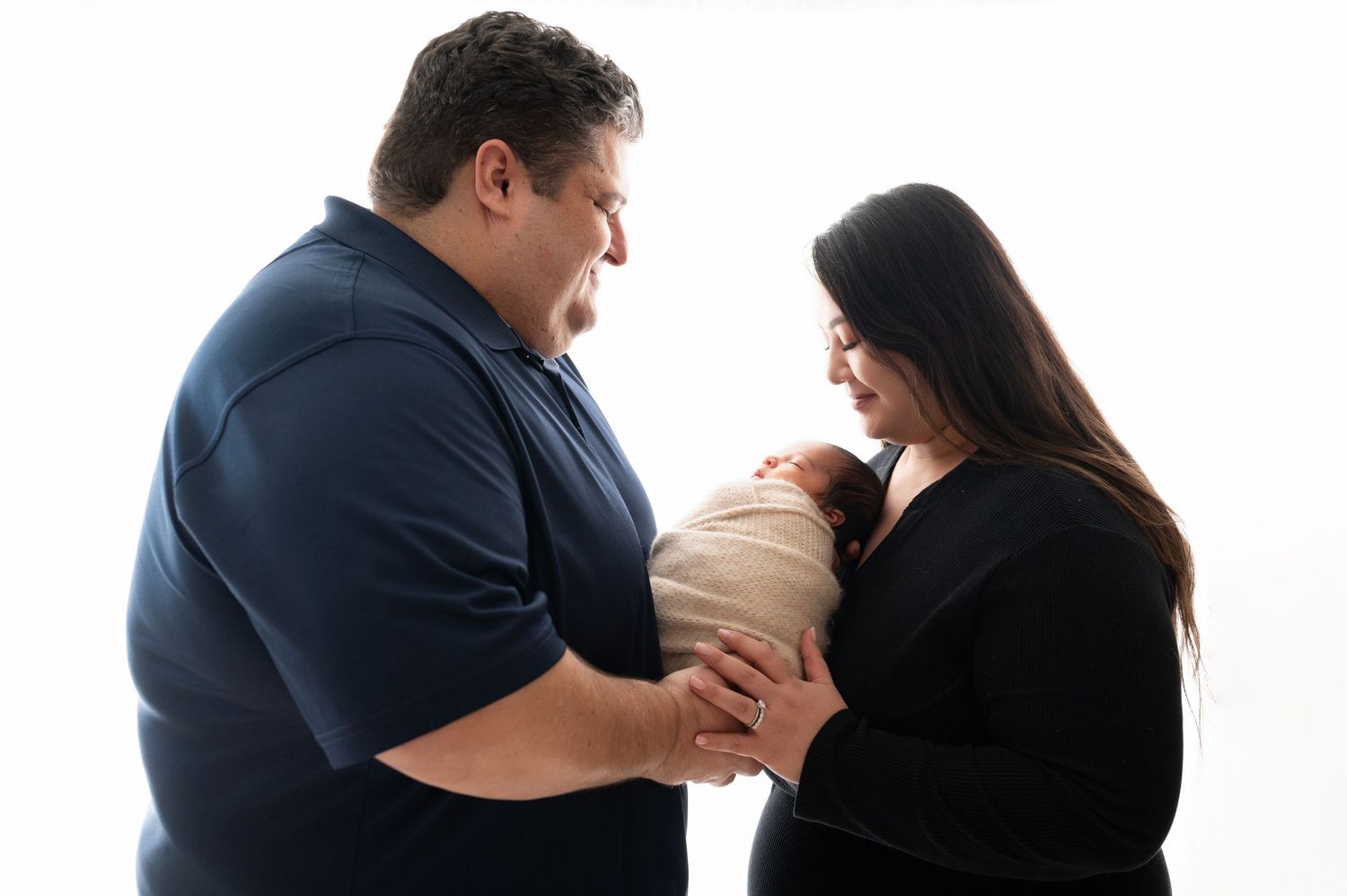 Parents sharing intimate moment while holding their swaddled newborn in studio setting.