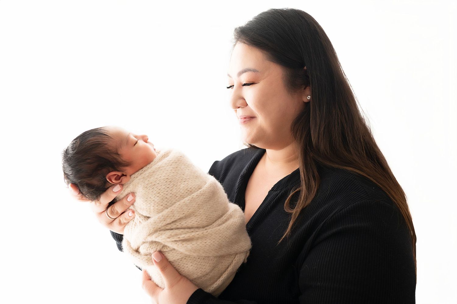 Parent in black top gazing lovingly at wrapped newborn during studio portrait session.